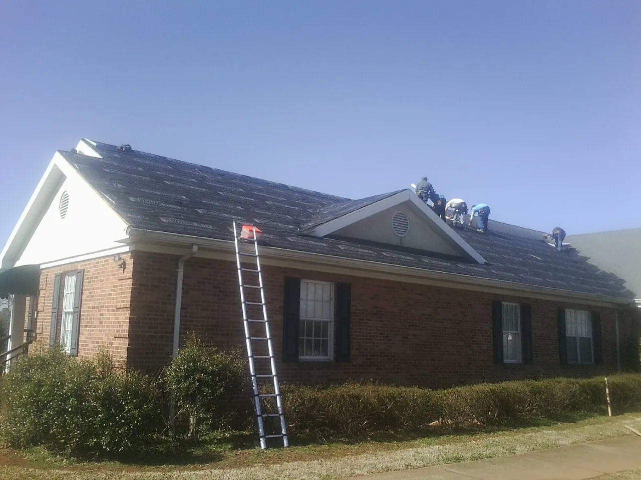 Crew tearing shingles off a brick ranch roof with a ladder set — Metal Roof Repair work by our crew in Indiana