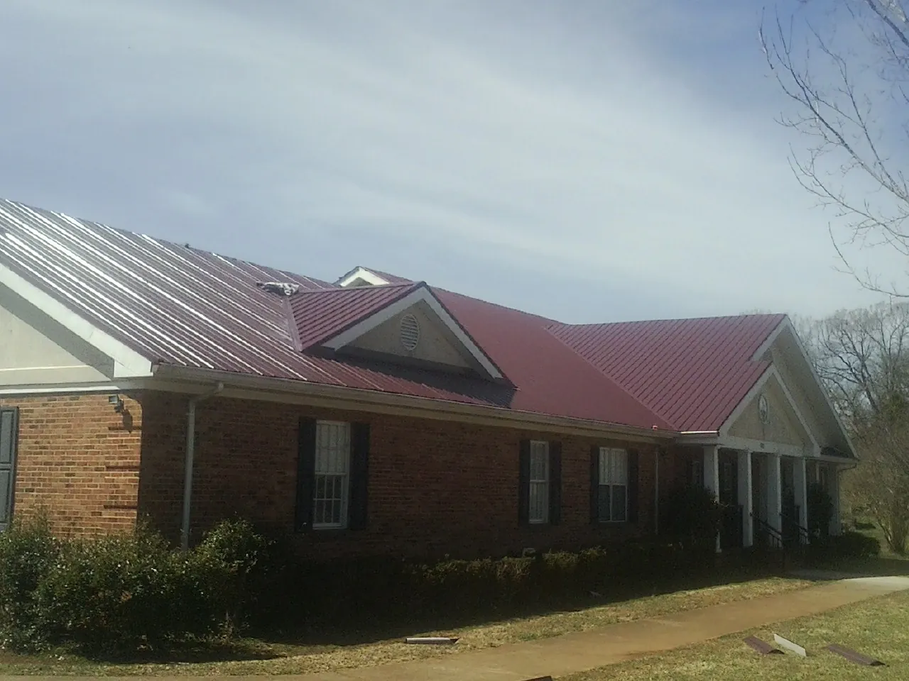 Red metal roof with gabled entries on a long brick building, from a Hail Damage Roof Repair job in Indiana