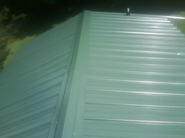 New green metal panels meeting at the ridge of a roof — Flat Roof Repair work by our crew in Indiana