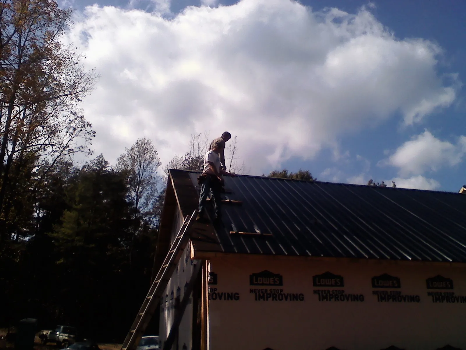 Roofer fastening dark metal panels high against a cloudy sky, from a Roof Inspection job in Indiana