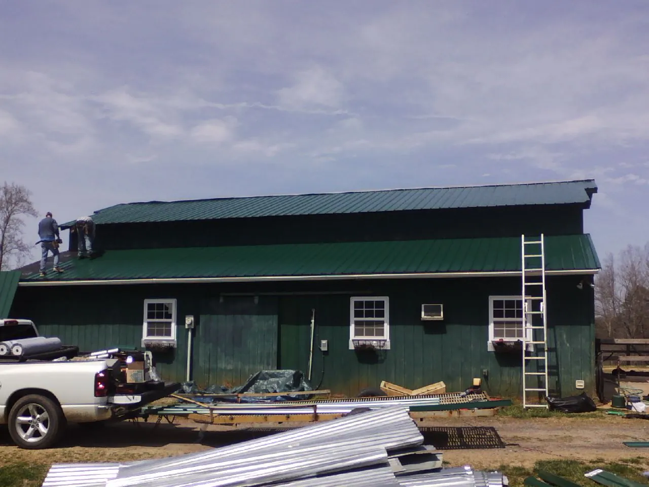 Crew installing green metal roofing on a large green barn in Indiana