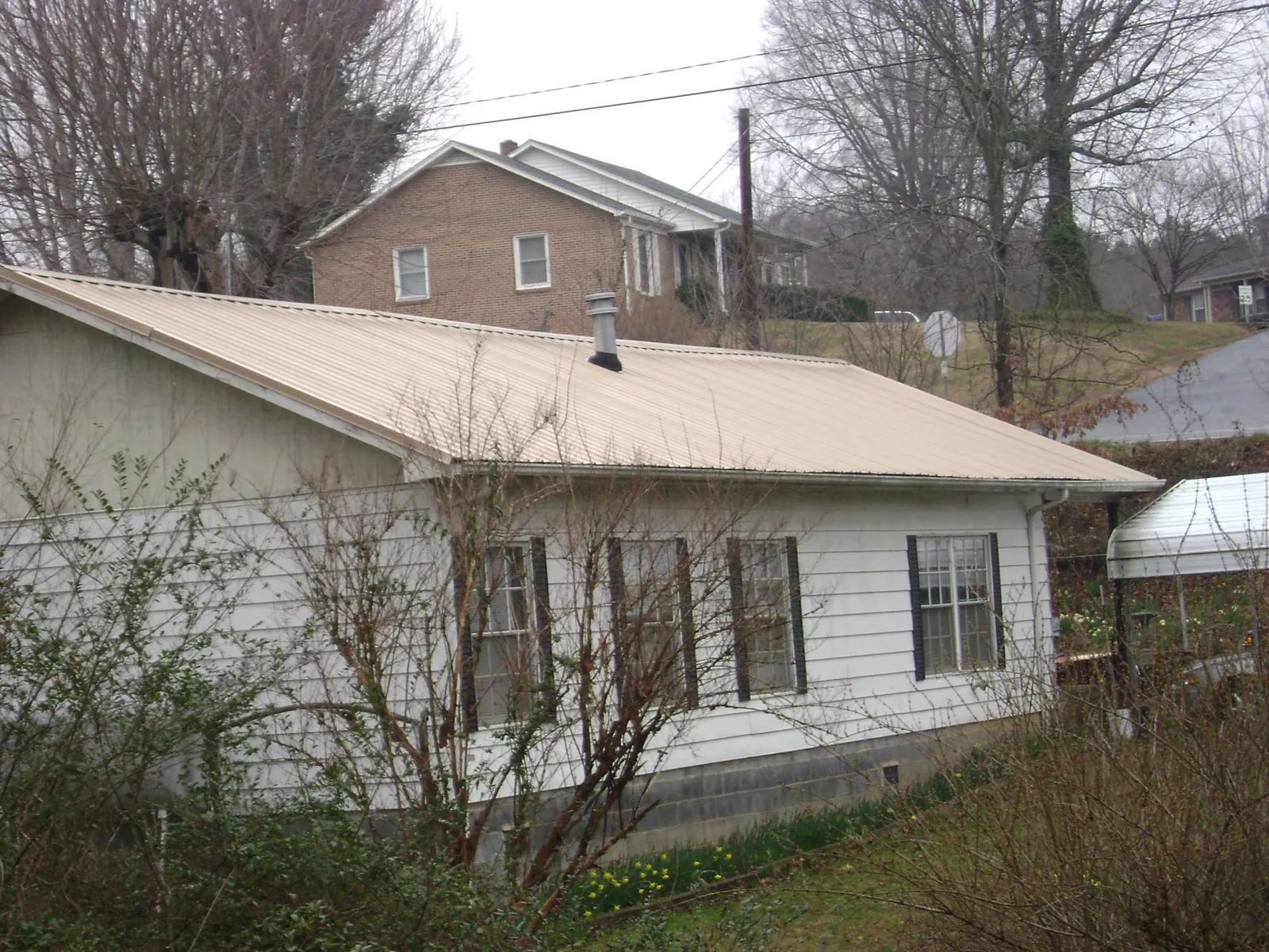 Tan metal roof on a white sided house set into a hillside — Commercial Roofing by Roofing Brothers in Indiana