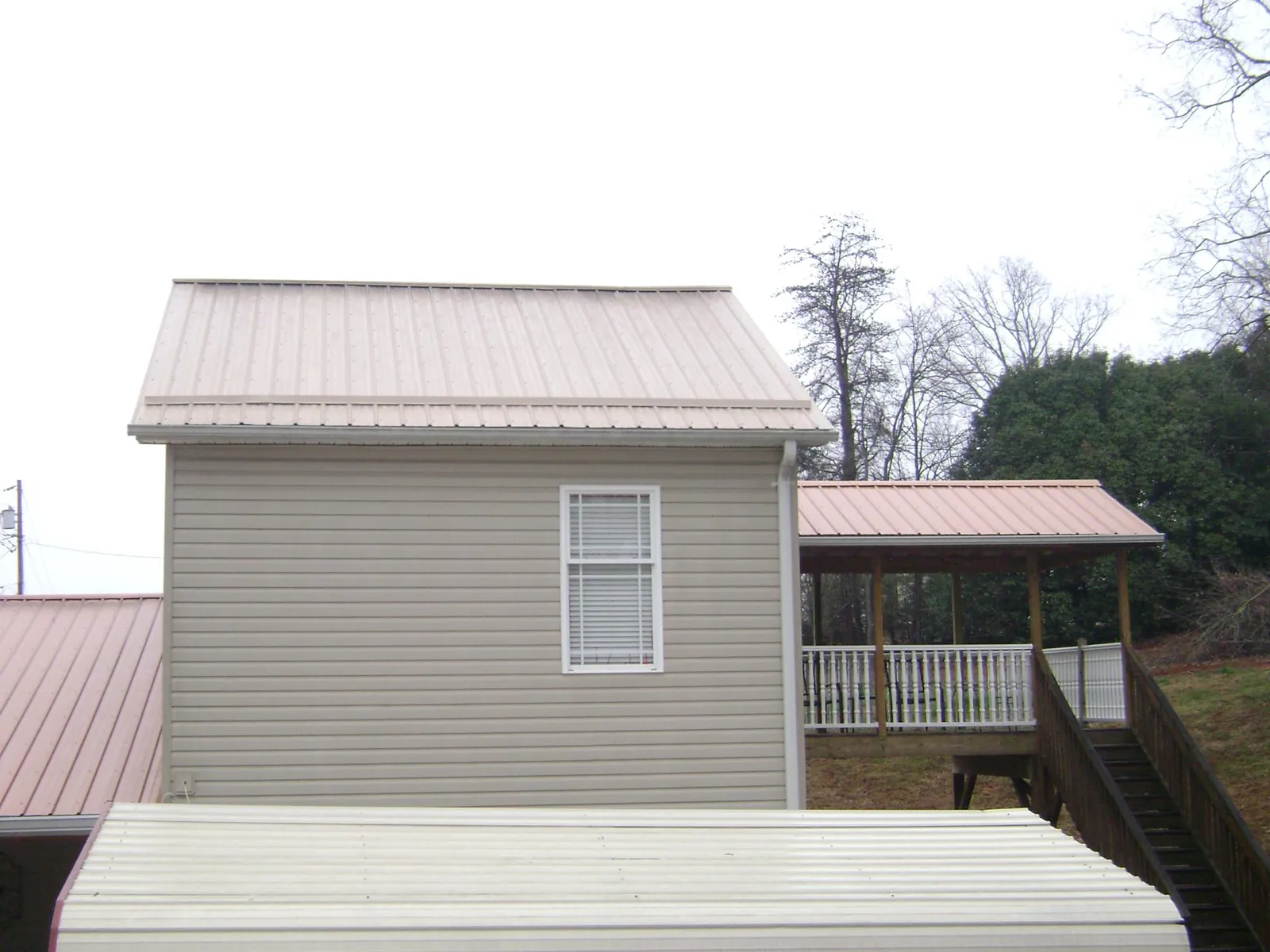 Tan metal roofs on a two story addition and attached porch, from a Roof Replacement job in Indiana